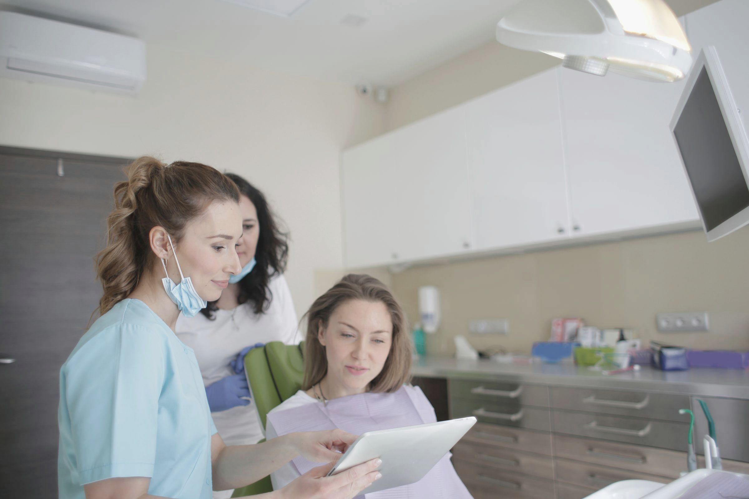 Dentalhygienikerin zeigt einer Patientin auf einem Tablet Bilder ihrer Zähne