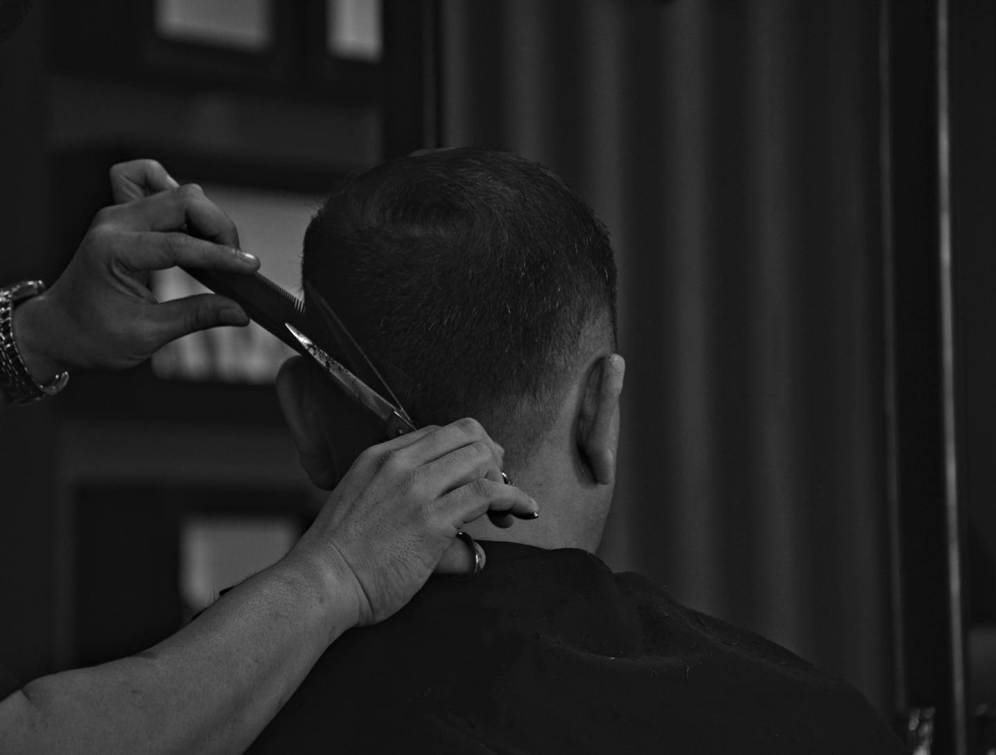 Barbier arbeitet mit Schere, Kamm und Maschine am Haar eines Gastes, Schwarzweissaufnahme