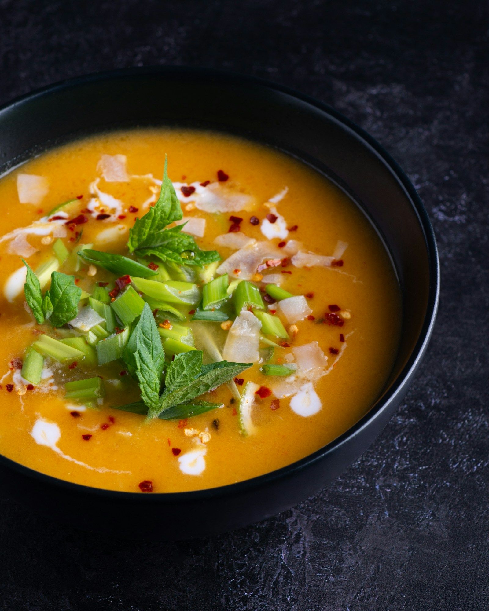 Kürbissuppe mit Kräutern in einer dunklen Schale